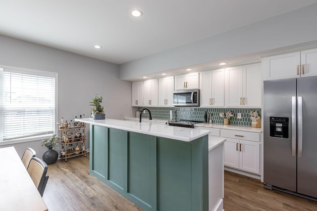 kitchen with backsplash, white cabinets, a center island with sink, light wood-type flooring, and appliances with stainless steel finishes