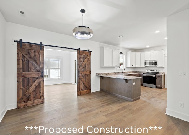 kitchen with white cabinets, a barn door, light stone countertops, appliances with stainless steel finishes, and kitchen peninsula