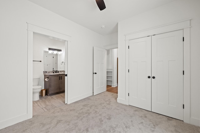 unfurnished bedroom with ceiling fan, sink, ensuite bathroom, light colored carpet, and a closet