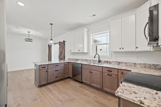 kitchen featuring stainless steel appliances, sink, a barn door, decorative light fixtures, and white cabinets