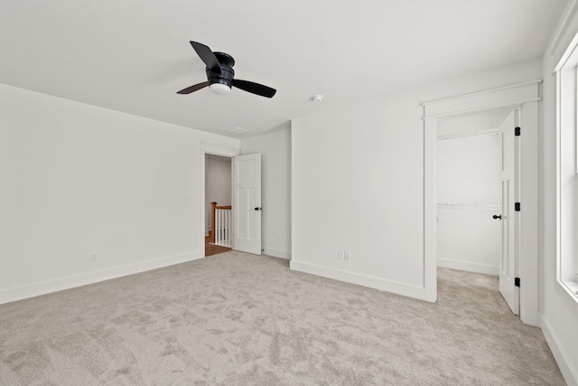 unfurnished bedroom with light carpet, a walk in closet, a closet, and ceiling fan