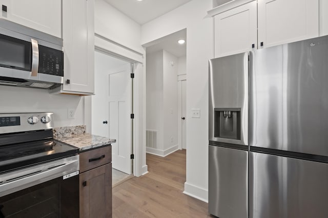 kitchen with white cabinets, appliances with stainless steel finishes, light wood-type flooring, and light stone counters