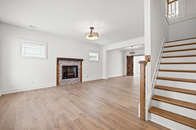 unfurnished living room featuring a barn door, light hardwood / wood-style floors, and a brick fireplace