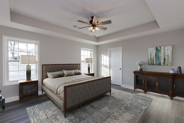 bedroom with ceiling fan, dark wood-type flooring, and a tray ceiling