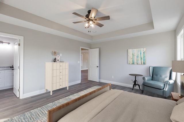 bedroom featuring a tray ceiling, ceiling fan, dark wood-type flooring, and ensuite bathroom