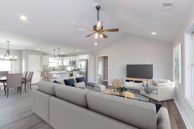 living room featuring ceiling fan with notable chandelier, wood-type flooring, sink, and vaulted ceiling