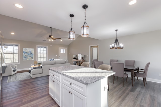 kitchen with light stone counters, ceiling fan with notable chandelier, dark wood-type flooring, white cabinetry, and hanging light fixtures