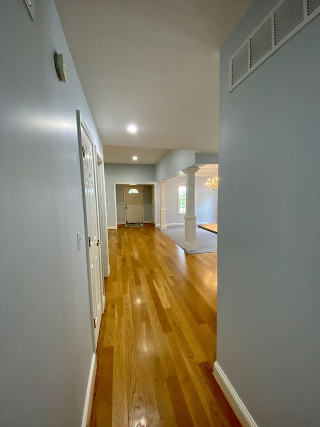 corridor featuring hardwood / wood-style flooring, ornate columns, and a notable chandelier