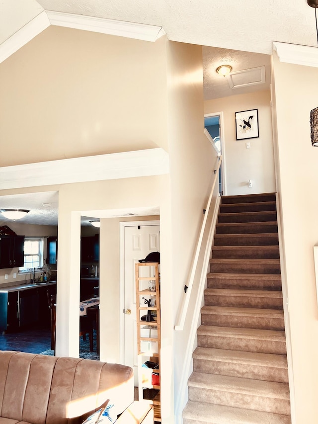 stairs featuring a textured ceiling, sink, lofted ceiling, and crown molding