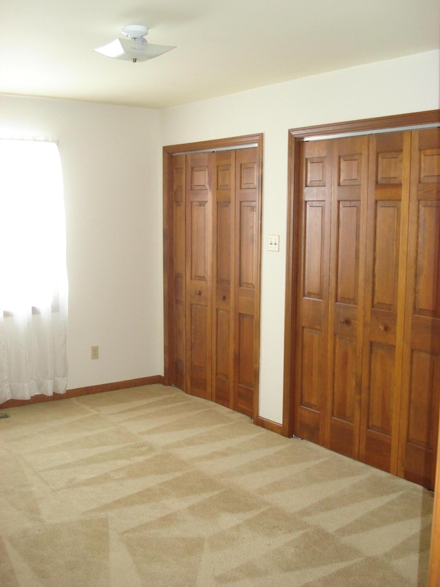 unfurnished bedroom featuring two closets, light colored carpet, and ceiling fan