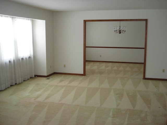 carpeted empty room with an inviting chandelier