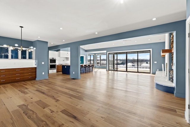 unfurnished living room with light wood-type flooring and an inviting chandelier