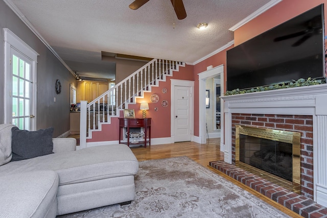 living room featuring a brick fireplace, ceiling fan, light wood-type flooring, a textured ceiling, and crown molding