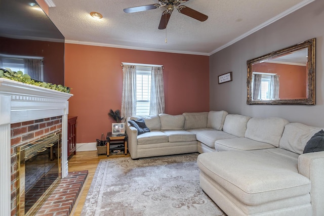 living room featuring ceiling fan, a fireplace, crown molding, hardwood / wood-style flooring, and a textured ceiling