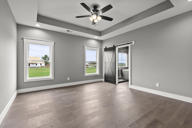 unfurnished room with wood-type flooring, a barn door, a raised ceiling, and ceiling fan