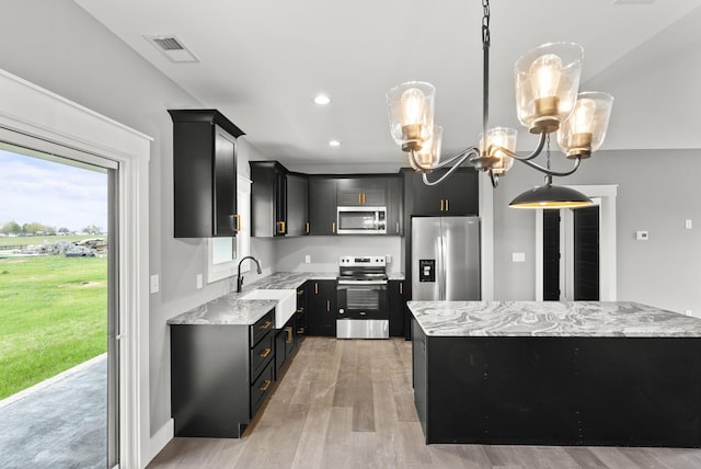 kitchen with sink, an inviting chandelier, light stone counters, decorative light fixtures, and appliances with stainless steel finishes