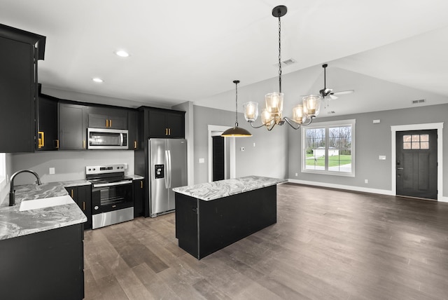 kitchen with light stone countertops, a center island, hanging light fixtures, ceiling fan with notable chandelier, and appliances with stainless steel finishes