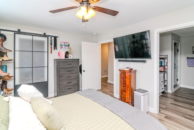 bedroom with ceiling fan, a barn door, and light hardwood / wood-style flooring