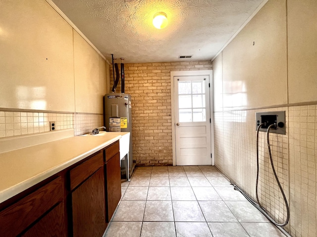 kitchen with light tile patterned floors, crown molding, water heater, tile walls, and a textured ceiling