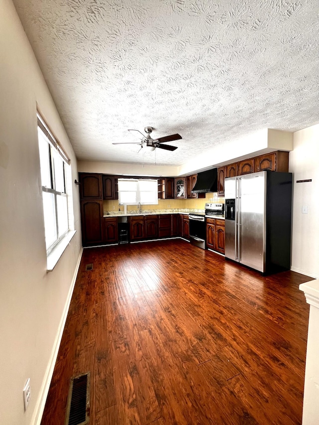 kitchen with wall chimney range hood, sink, ceiling fan, appliances with stainless steel finishes, and dark hardwood / wood-style floors