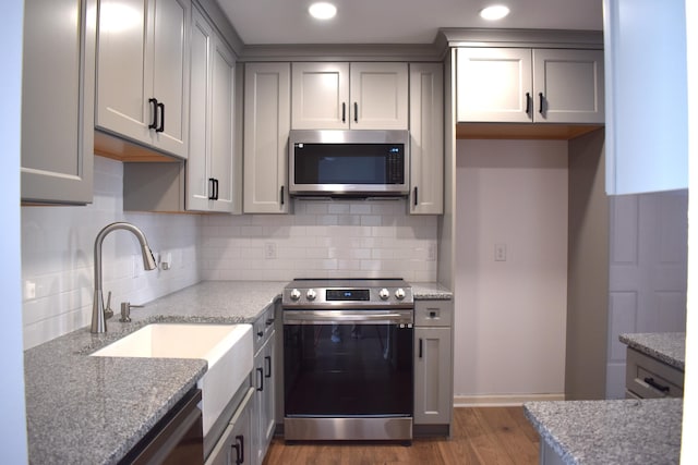 kitchen with appliances with stainless steel finishes, backsplash, light stone counters, gray cabinetry, and dark hardwood / wood-style floors