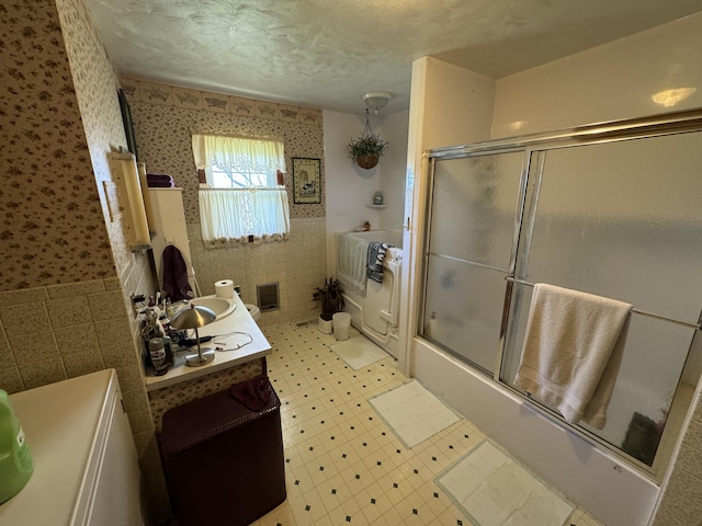 bathroom featuring combined bath / shower with glass door, a textured ceiling, and vanity