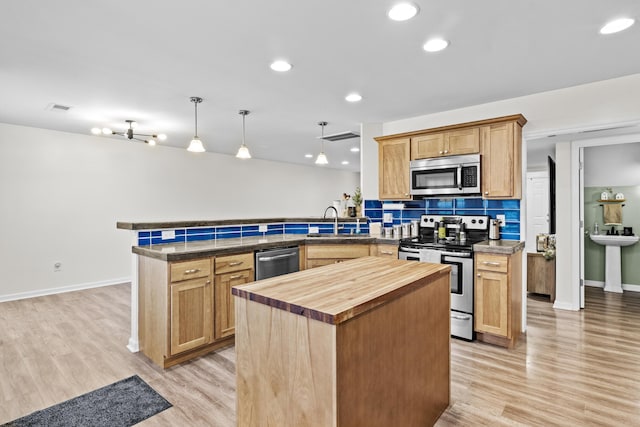 kitchen with wooden counters, appliances with stainless steel finishes, kitchen peninsula, pendant lighting, and a center island