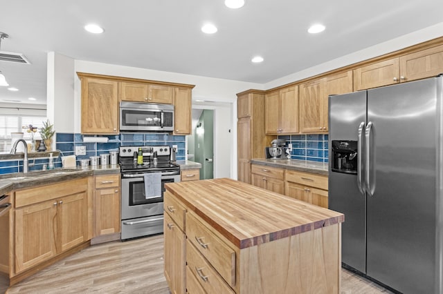 kitchen with tasteful backsplash, stainless steel appliances, sink, light hardwood / wood-style flooring, and a kitchen island