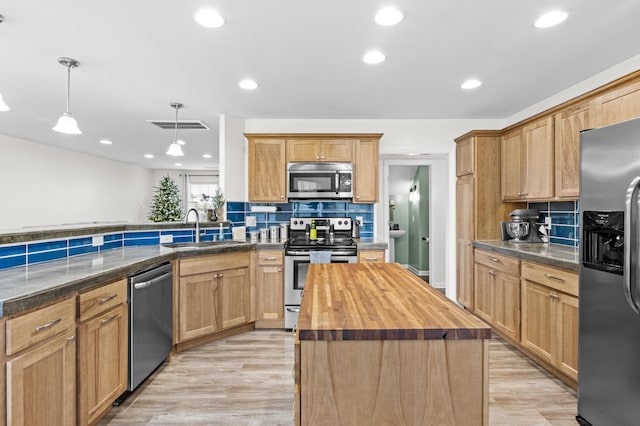 kitchen featuring appliances with stainless steel finishes, light hardwood / wood-style flooring, a center island, hanging light fixtures, and butcher block counters