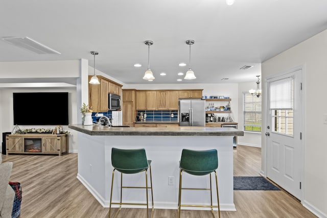 kitchen featuring pendant lighting, stainless steel refrigerator with ice dispenser, tasteful backsplash, light hardwood / wood-style floors, and a kitchen bar