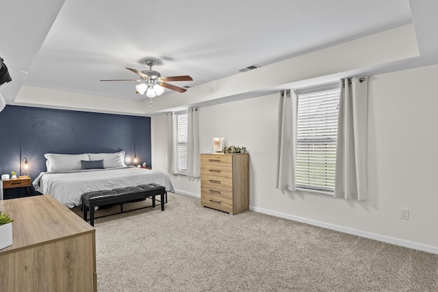 bedroom with ceiling fan, light carpet, and a tray ceiling