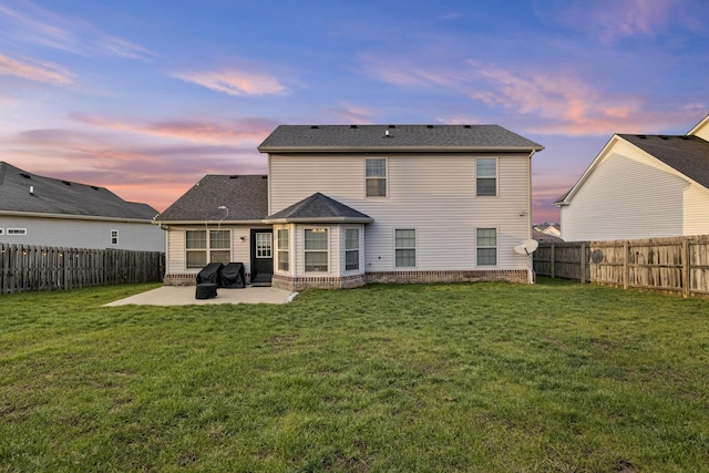 back house at dusk with a patio and a lawn