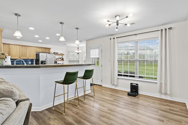 kitchen with light wood-type flooring, stainless steel refrigerator with ice dispenser, hanging light fixtures, and an inviting chandelier