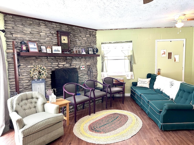 living room featuring dark hardwood / wood-style flooring, ceiling fan, a stone fireplace, and a textured ceiling