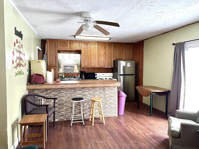 kitchen with a textured ceiling, dark wood-type flooring, stainless steel refrigerator, and kitchen peninsula