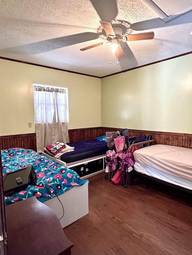 bedroom featuring dark hardwood / wood-style floors, wooden walls, ornamental molding, ceiling fan, and a textured ceiling