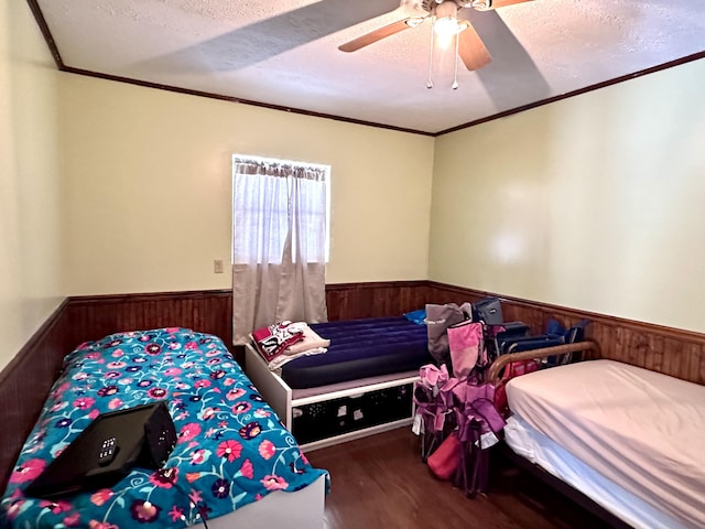 bedroom with hardwood / wood-style floors, wooden walls, ornamental molding, ceiling fan, and a textured ceiling