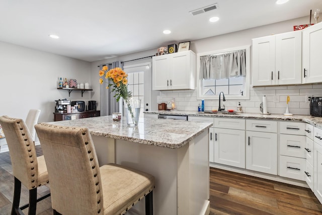 kitchen featuring a kitchen island, white cabinetry, light stone counters, and a breakfast bar area