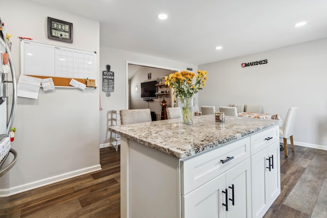 kitchen with a center island, white cabinetry, dark wood-type flooring, and light stone counters