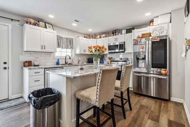 kitchen with white cabinets, appliances with stainless steel finishes, a center island, and dark hardwood / wood-style flooring