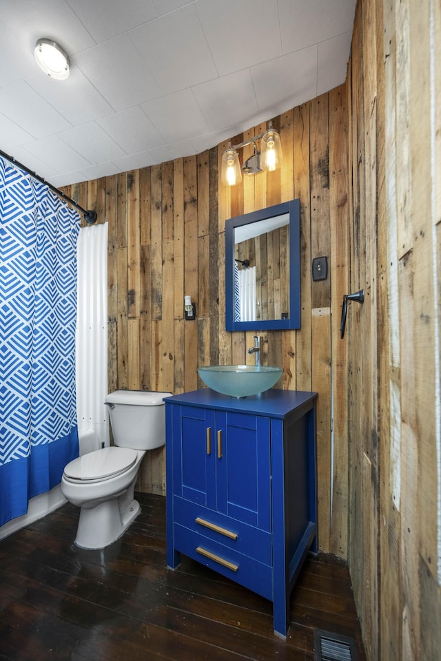 bathroom featuring visible vents, toilet, wooden walls, vanity, and hardwood / wood-style flooring