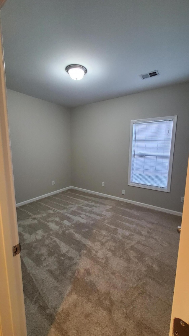 unfurnished room featuring visible vents, dark carpet, and baseboards