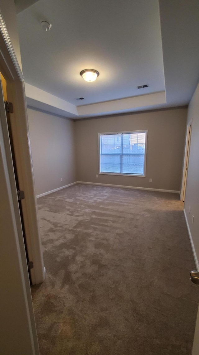 unfurnished room featuring a tray ceiling, baseboards, visible vents, and dark colored carpet