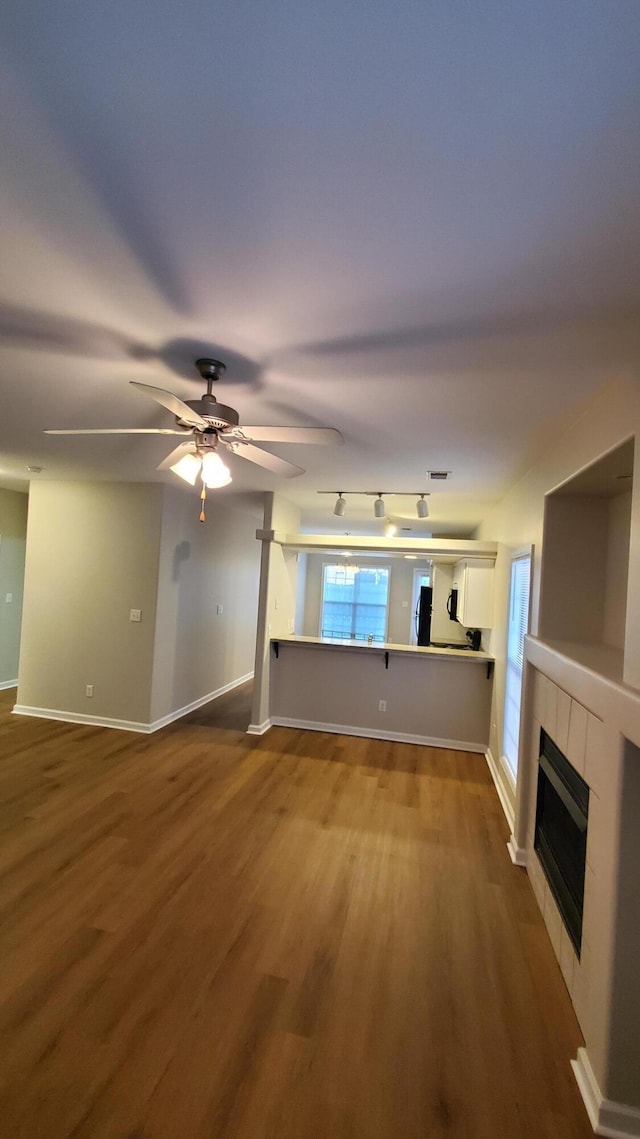 unfurnished living room featuring a tiled fireplace, baseboards, ceiling fan, and wood finished floors