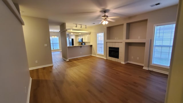 unfurnished living room with visible vents, baseboards, a tile fireplace, a ceiling fan, and dark wood-style flooring