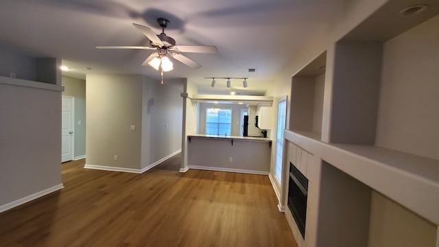 unfurnished living room featuring a ceiling fan, wood finished floors, baseboards, a fireplace, and track lighting