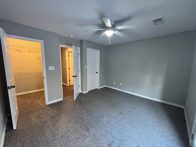 unfurnished bedroom featuring ceiling fan, a spacious closet, a closet, and dark colored carpet