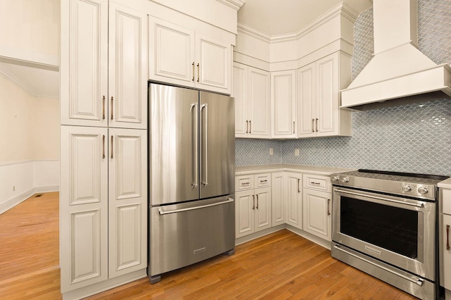 kitchen featuring decorative backsplash, appliances with stainless steel finishes, custom range hood, crown molding, and light hardwood / wood-style floors