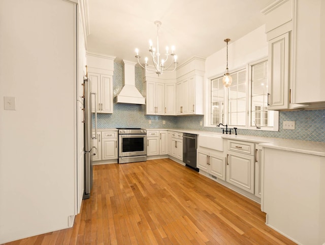 kitchen with white cabinetry, sink, stainless steel appliances, decorative light fixtures, and custom range hood