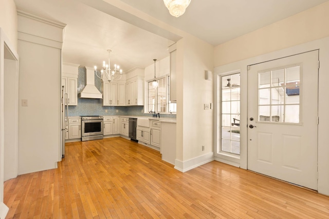 kitchen featuring appliances with stainless steel finishes, backsplash, custom range hood, pendant lighting, and an inviting chandelier